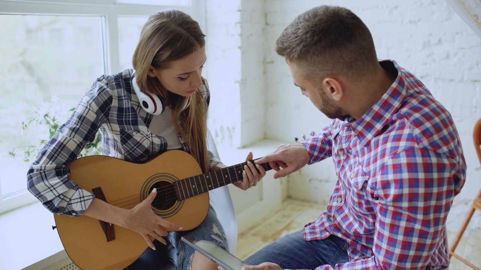 Lehrerin zeigt einer Jugendlichen Griffe auf der Gitarre im sonnigen Raum